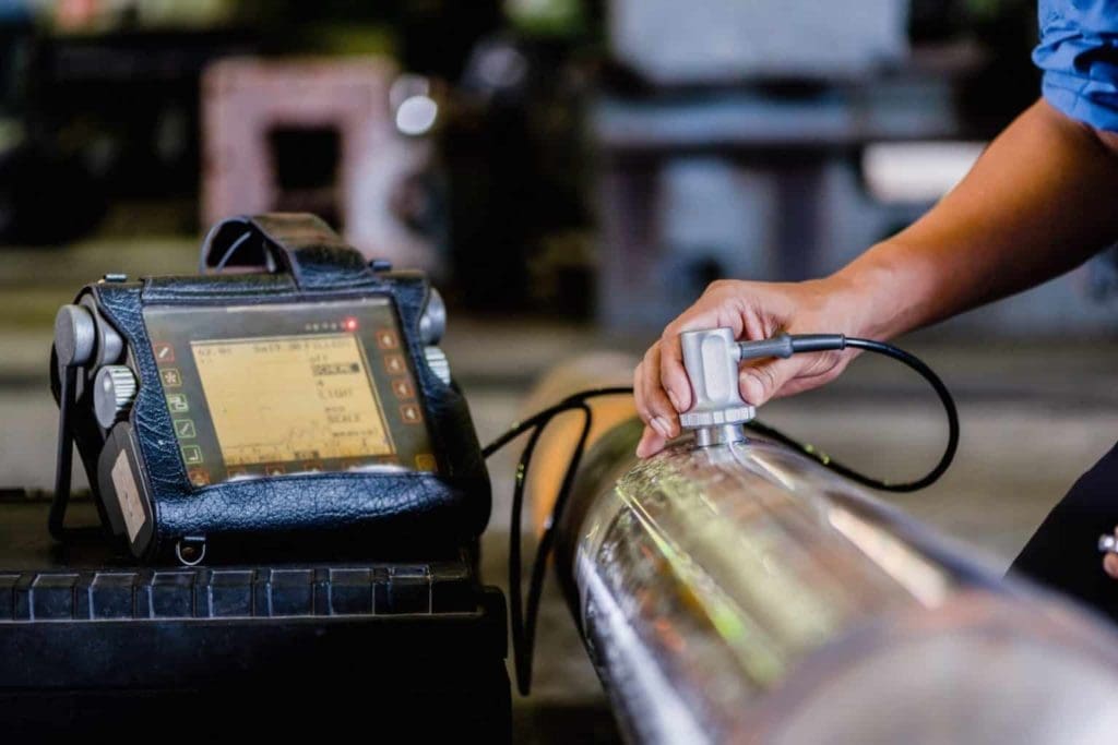 Technician performing ultrasonic test to detect imperfection or defect of round metal pipe